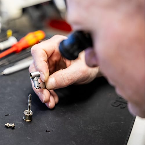 Nærbillede af en tekniker, der reparerer et dentalinstrument med præcisionsværktøj Nærbillede af en tekniker, der reparerer et dentalinstrument med præcisionsværktøj