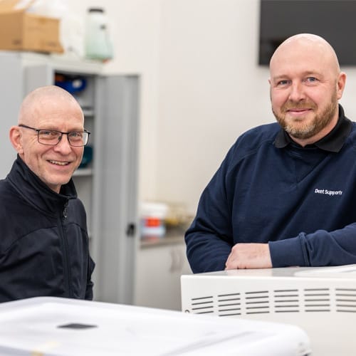 To smilende serviceteknikere fra Dent Support i værkstedet To smilende serviceteknikere fra Dent Support i værkstedet